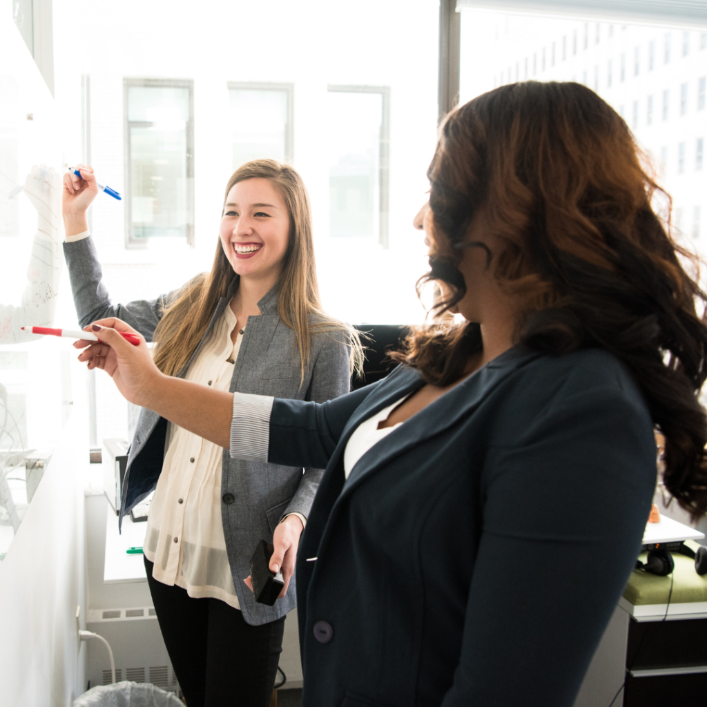 Two women working together in a K12 business environment, they're collaborating on something successful like increasing alumni engagement. two women working on marketing materials for their local K12 school's social media account could help inspire others. .