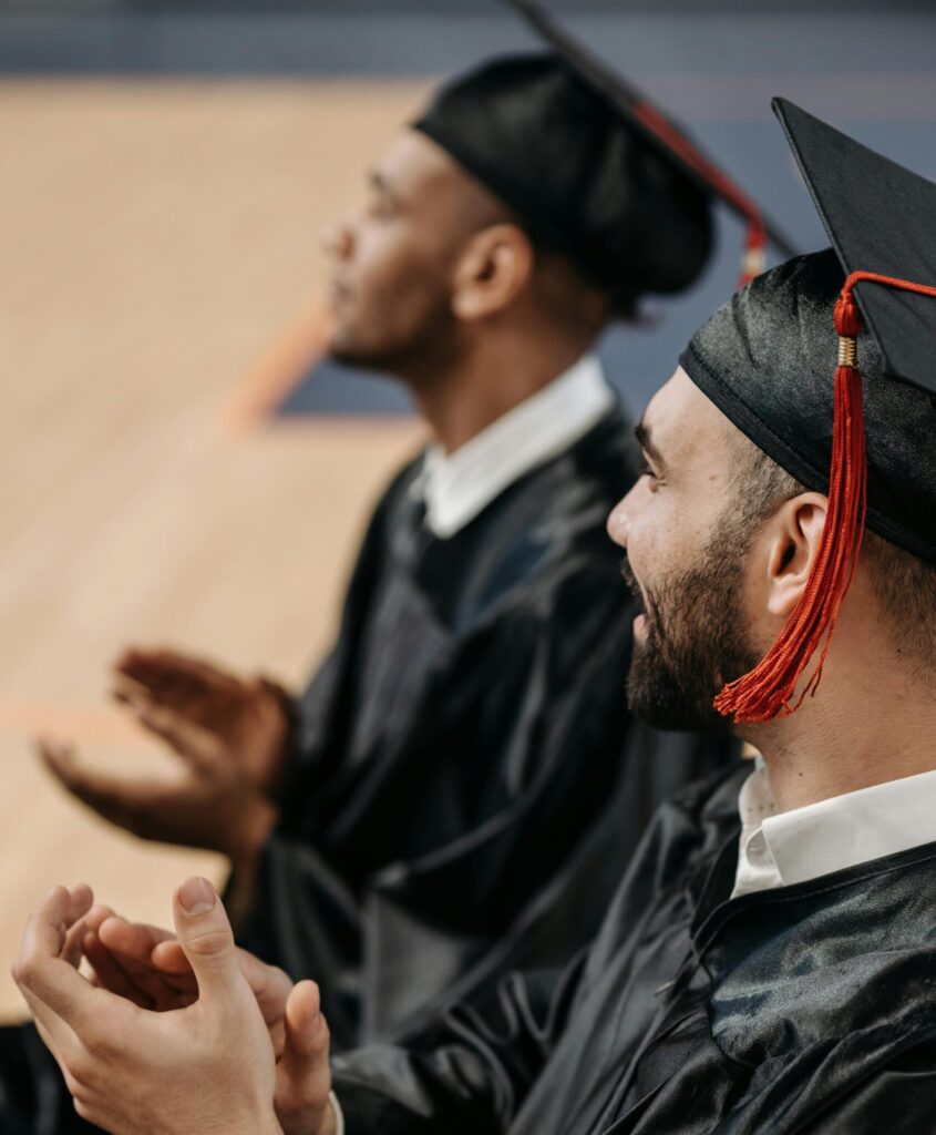 Two men wearing graduation caps and gowns clap