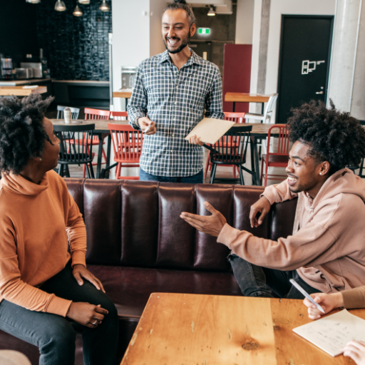  3 People in a restaurant at a booth conversing amongst themselves in a group. 