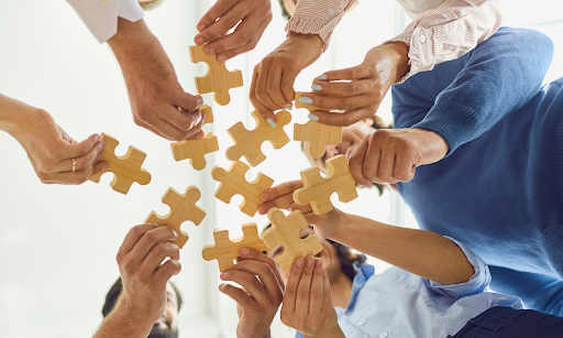 A group of people placing pieces of a puzzle together representing the group effort of alumni to bring together a community for their K12 schools.