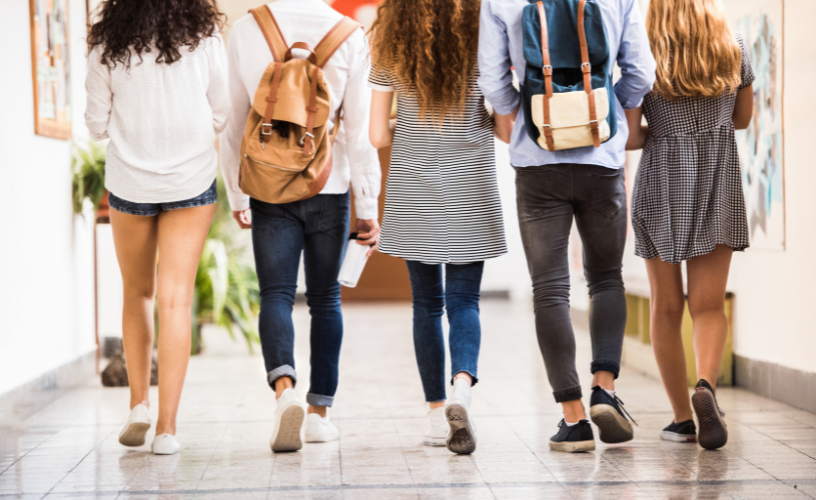 Five high schoolers walking in a school hallway.