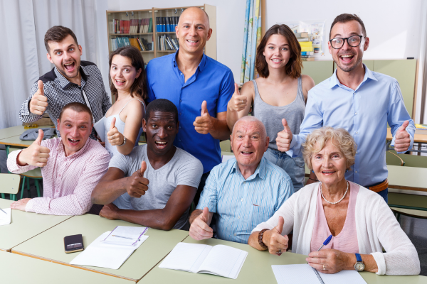 Diverse group of alumni volunteers of various ages giving thumbs up in a classroom setting during a school giving campaign