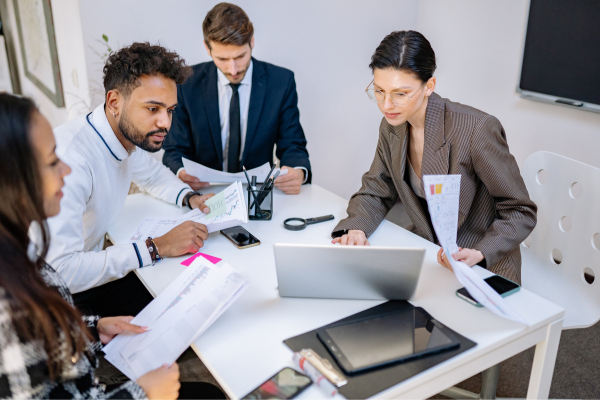 Alt Text- Four People in a conference room looking over plans for a database.