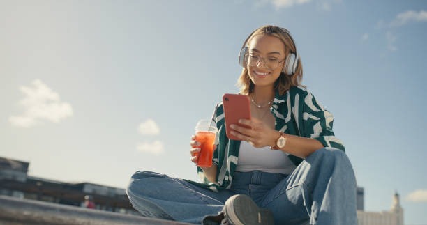 Young female alumni scrolling on her phone outdoors on a sunny summer day