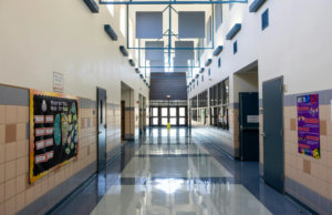 Empty school hallway with high ceilings, bulletin boards, and sunlight reflecting on polished floors.