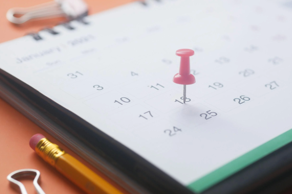 Close-up of a desk calendar with a push pin marking a specific date, alongside a pencil and binder clip.