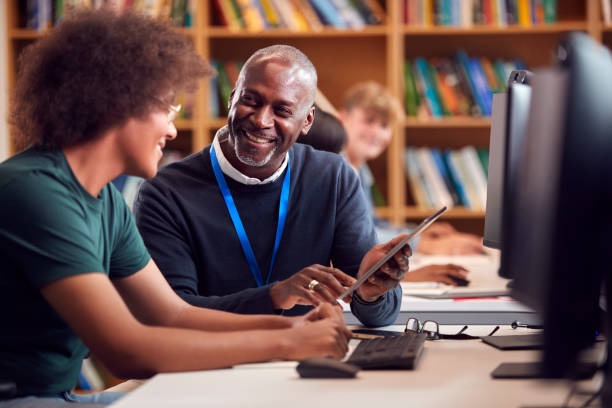 Adult mentor reviewing a project with a high school student in a classroom.