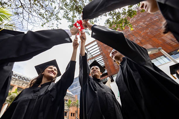 Group of high school graduates raising their diplomas together in celebration after commencement